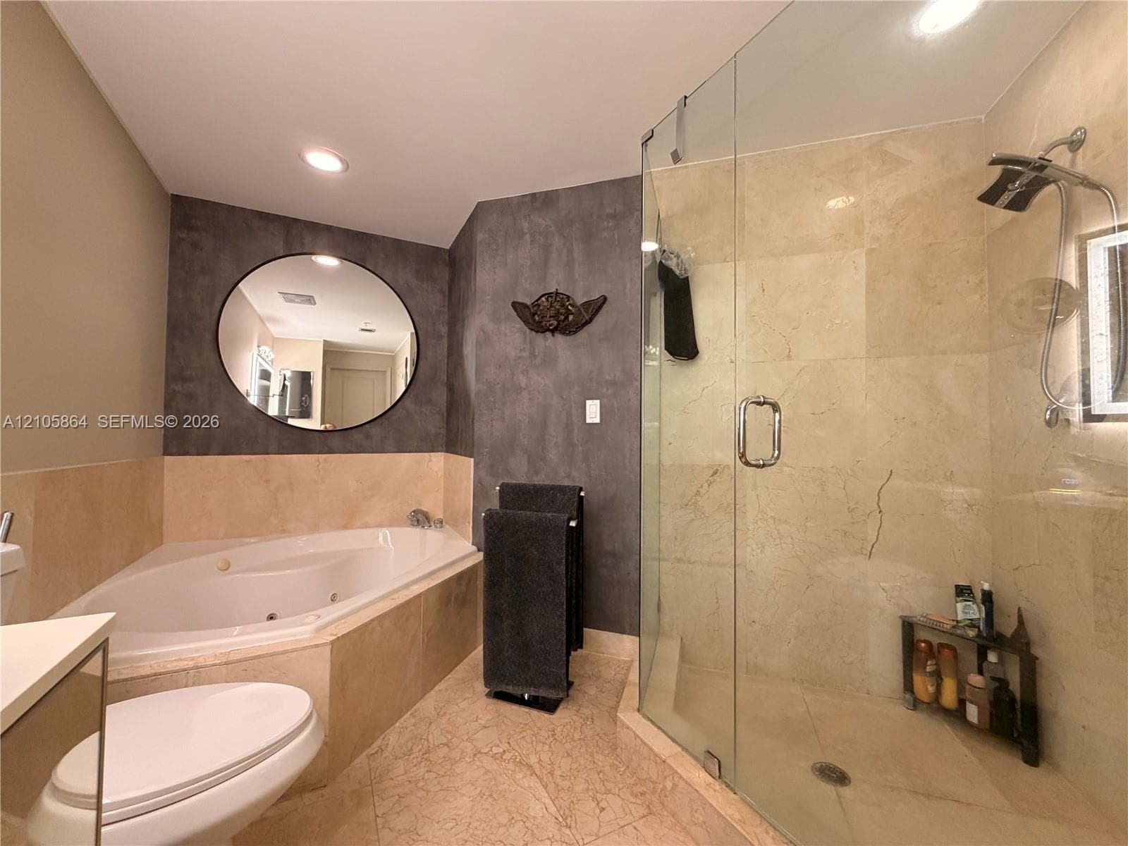 Jetted corner soaking tub, walk-in glass-enclosed shower with stone-finish tiling, and circular wall-mounted mirror