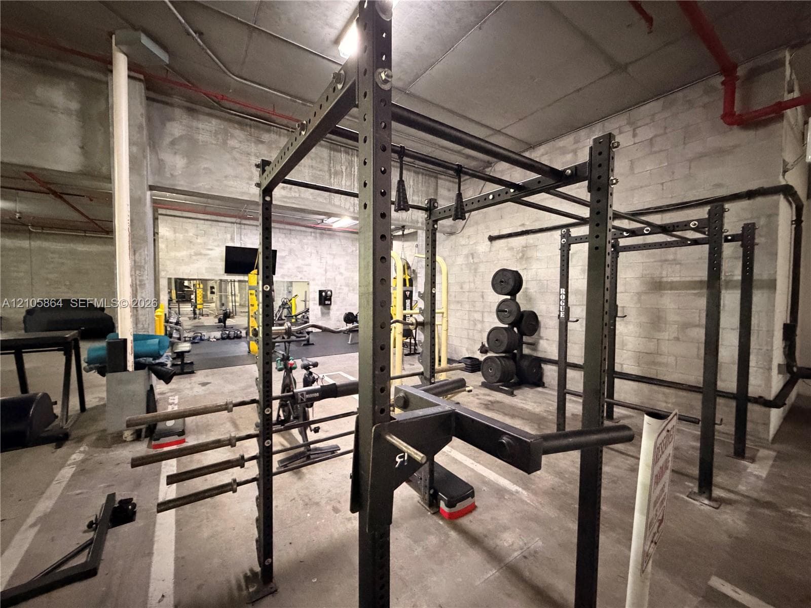 Industrial-style fitness space featuring concrete block walls, exposed structural elements, and concrete flooring