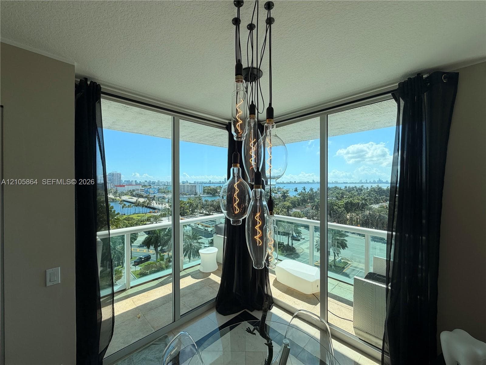 Floor-to-ceiling corner windows with sliding glass doors, multi-pendant Edison-style light fixture, and wraparound balcony with metal railing