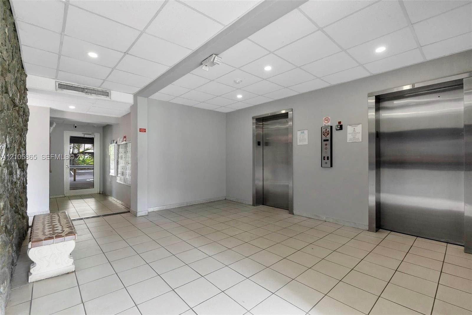 Lobby area featuring large-format tile flooring, dual stainless steel elevators, recessed lighting, and a textured natural stone accent wall
