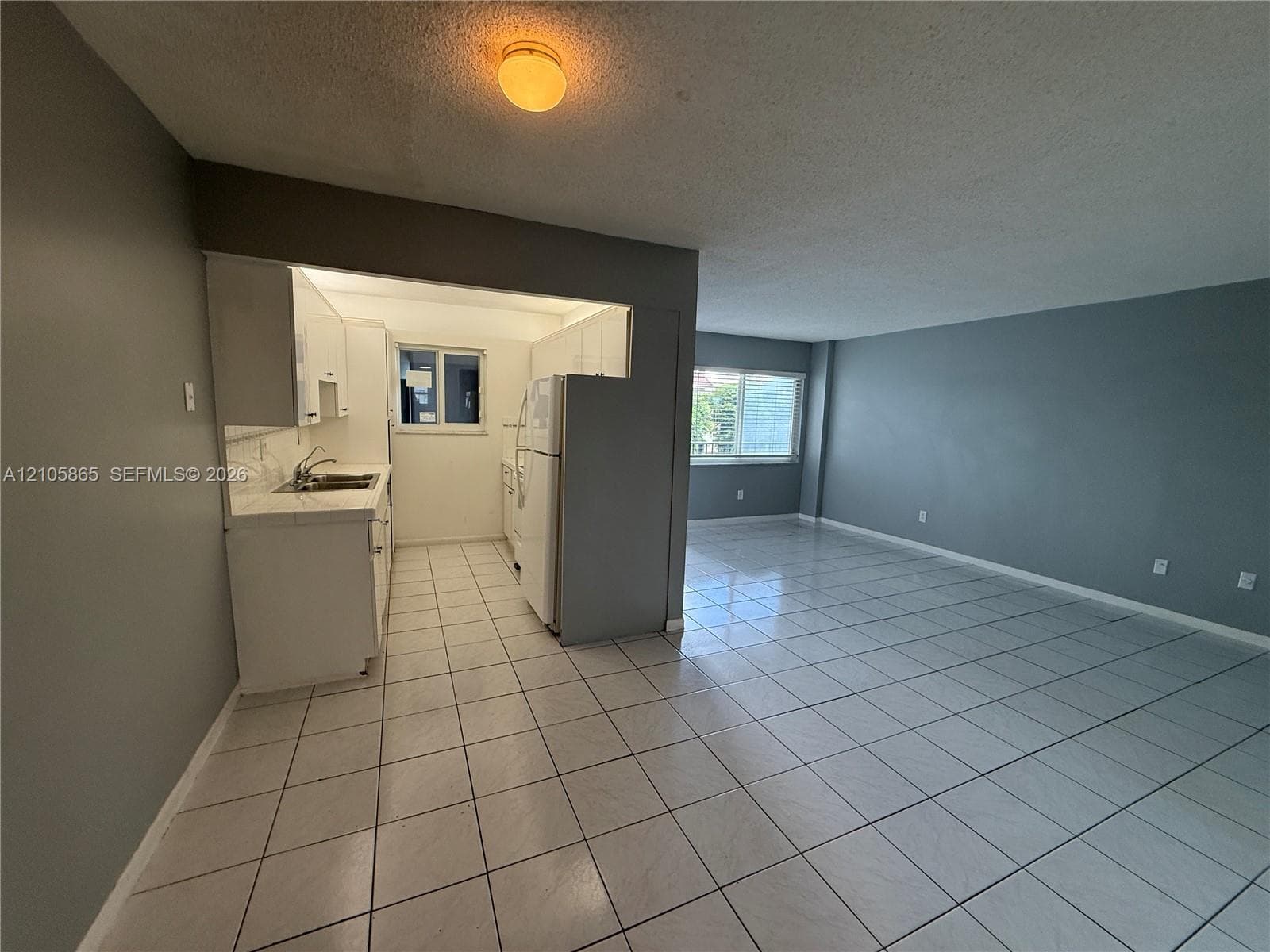 Interior space featuring uniform ceramic tile flooring, kitchen with white cabinetry, dual-basin sink, and natural light via windows