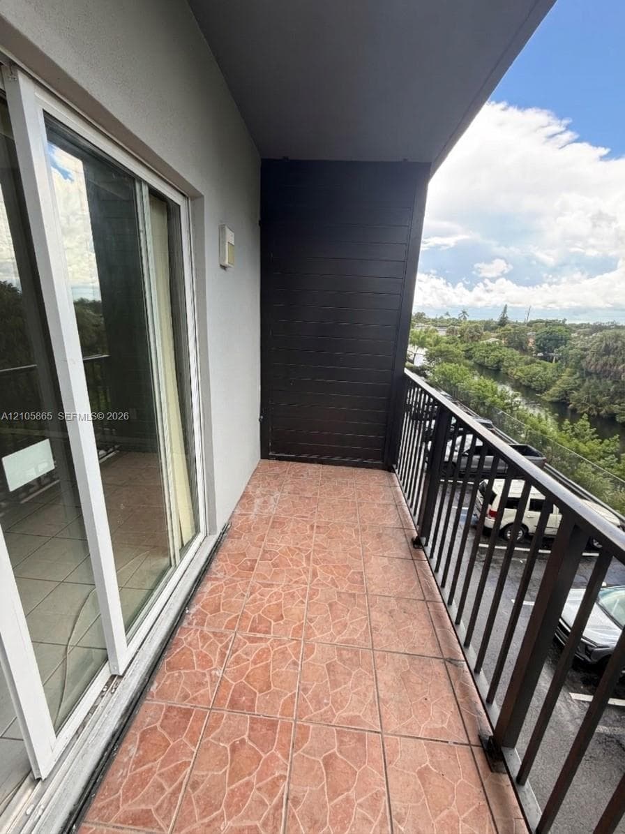 Covered balcony featuring multi-tonal stone-tile flooring, dark horizontal wood-plank accent siding, and black metal railings