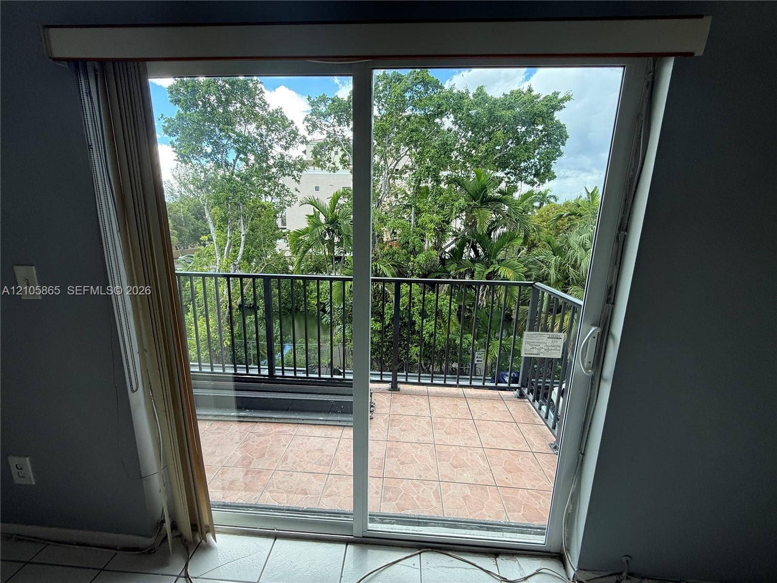 Sliding glass door opening to a private balcony featuring terracotta-style tile flooring and a black metal railing