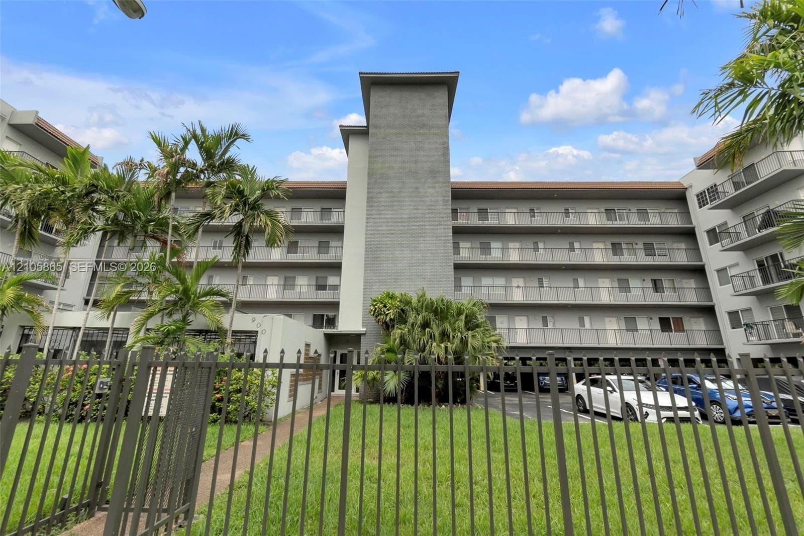 Multi-story exterior featuring a gray stucco facade, tiered balconies with metal railings, and a fenced perimeter
