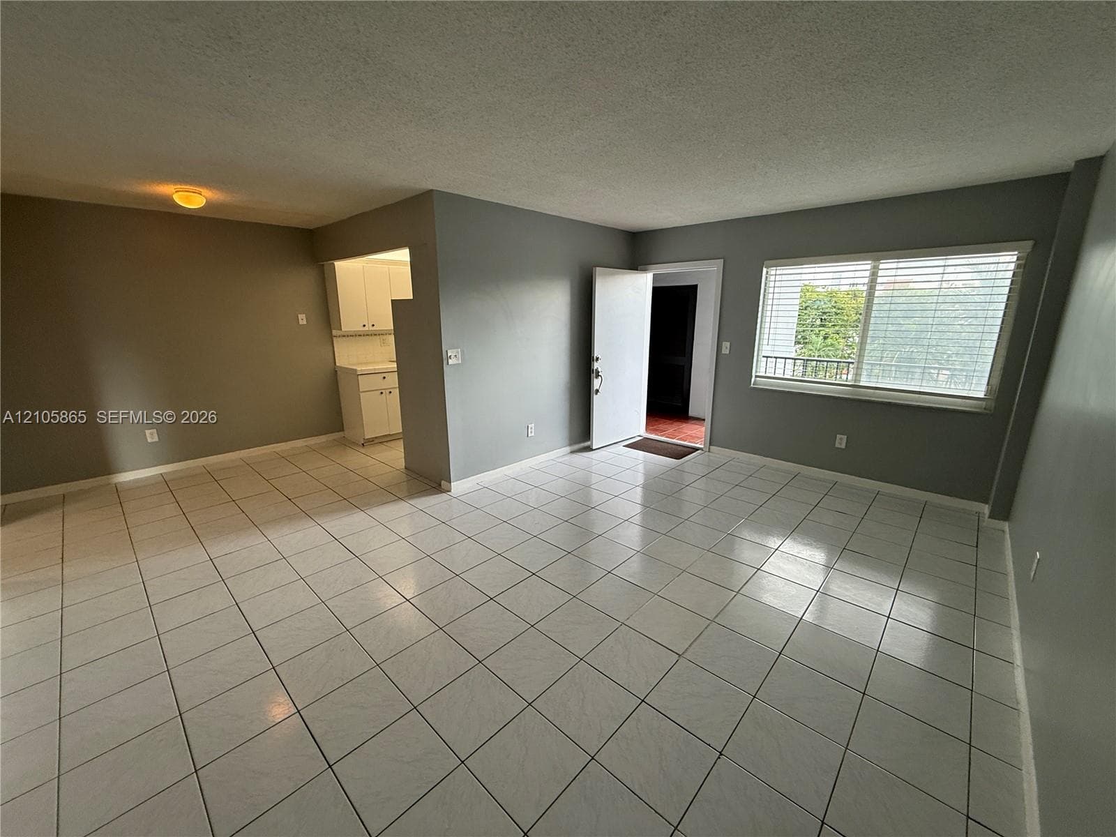 Neutral-toned interior featuring large-format white tile flooring, white cabinetry with recessed-panel doors, and a window with horizontal blinds
