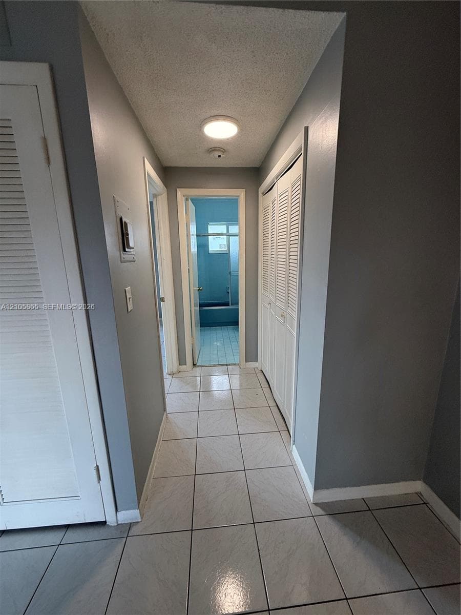 Hallway featuring white ceramic floor tiling, flush-mount lighting, and dual louvered-door closets
