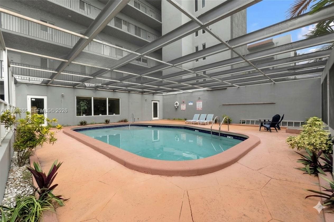 Swimming pool enclosed by a screen structure, surrounded by a paved deck featuring stone-texture surfacing and built-in metal handrails