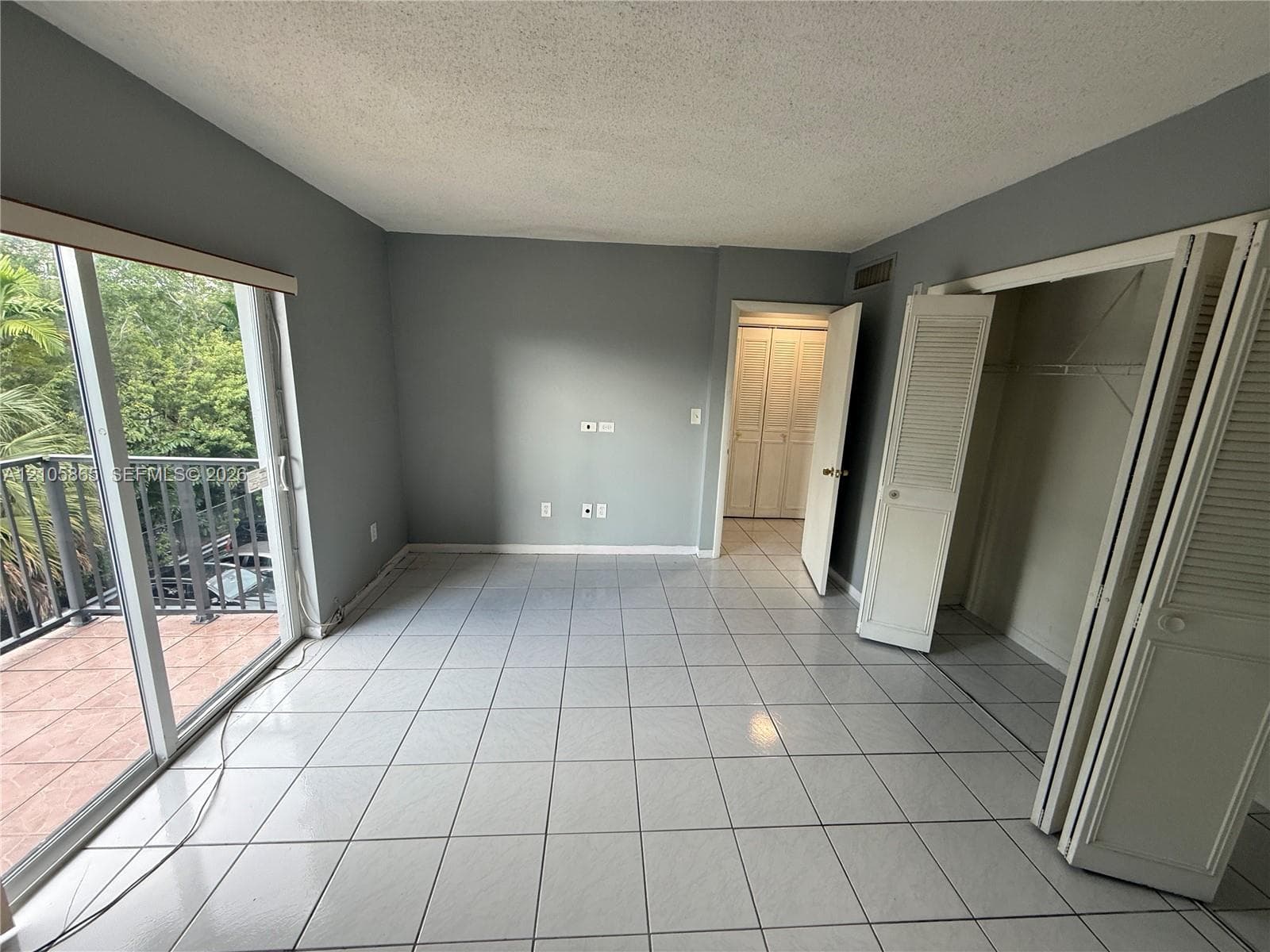 Interior room featuring ceramic tile flooring, sliding glass doors to a balcony, and dual bi-fold closet doors