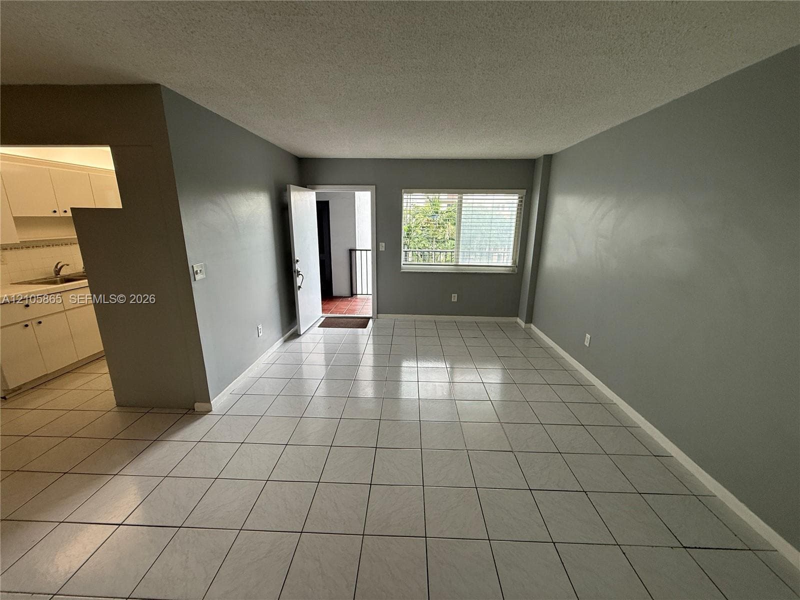 Open-concept interior featuring light-toned tile flooring, neutral wall paint, and a sliding window with horizontal blinds