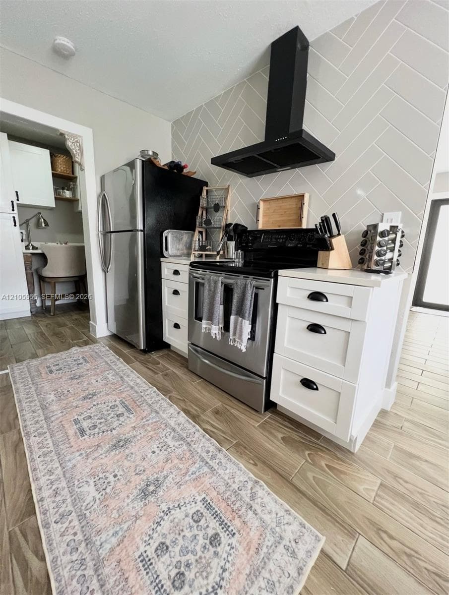 Main House Kitchen featuring white shaker-style cabinetry with matte black hardware, herringbone-patterned wall tile, stainless steel appliances, and wood-finish flooring