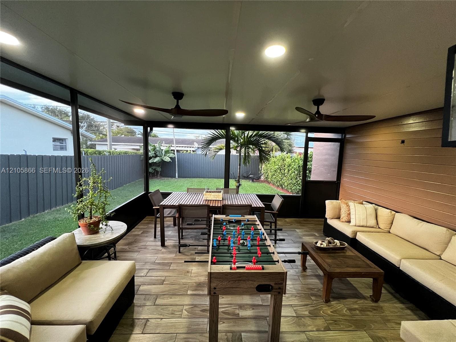 Main house patio and view of yard - Screened patio featuring wood-finish tile flooring, horizontal slat wall paneling, dual ceiling fans, and integrated recessed lighting