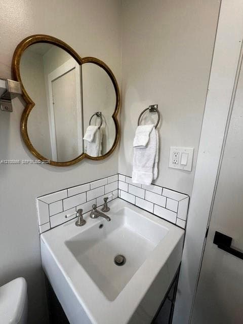 1/1 Private bathroom featuring a white ceramic corner sink with polished chrome faucet and fixtures, subway tile backsplash, decorative wood-framed mirror with arched detailing, and chrome towel bars