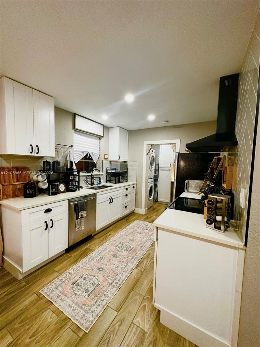 Main House Kitchen featuring white cabinetry, wood-finish flooring, a herringbone-patterned tile backsplash, a black range hood, and stainless steel appliances