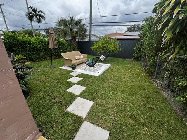 Private backyard featuring a manicured lawn, concrete paver pathway, elevated concrete patio, mature palms, and opaque perimeter fencing