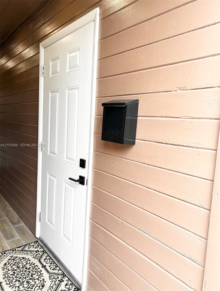 1/1 entry door Six-panel white entry door with matte black lever handle and electronic keypad deadbolt, complemented by horizontal lap siding and a wall-mounted metal mailbox