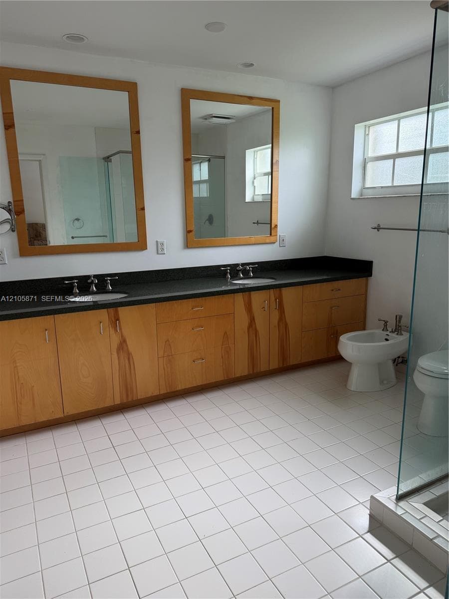 Dual-sink vanity with wood-finish cabinetry, dark solid-surface countertop, twin wood-framed mirrors, and a glass-enclosed shower