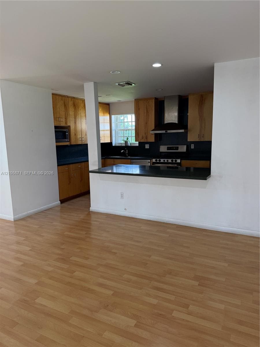 Kitchen featuring wood cabinetry, solid-surface countertops, breakfast bar, stainless steel range hood, and wood-finish flooring