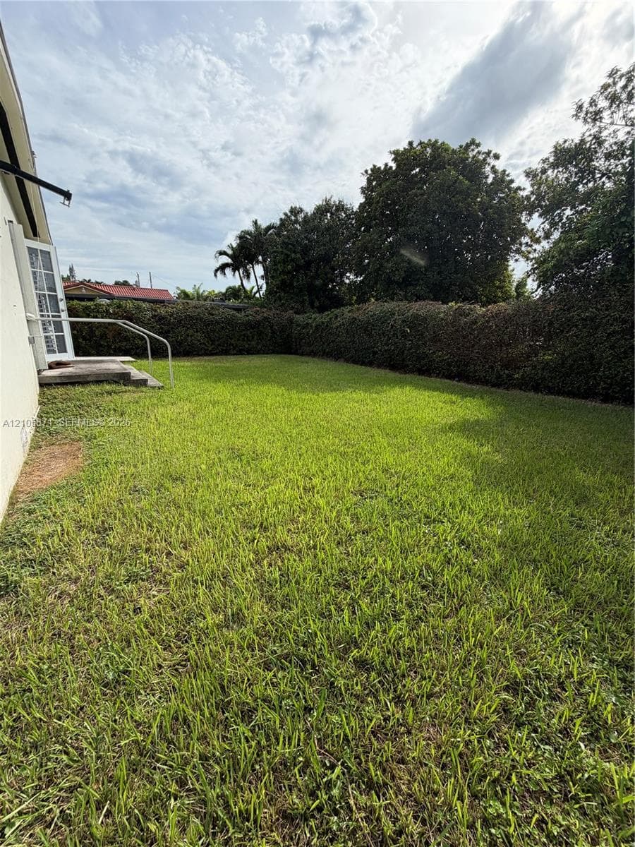 Private backyard featuring a level grass lawn, high perimeter hedges, and a concrete entry step with a metal handrail