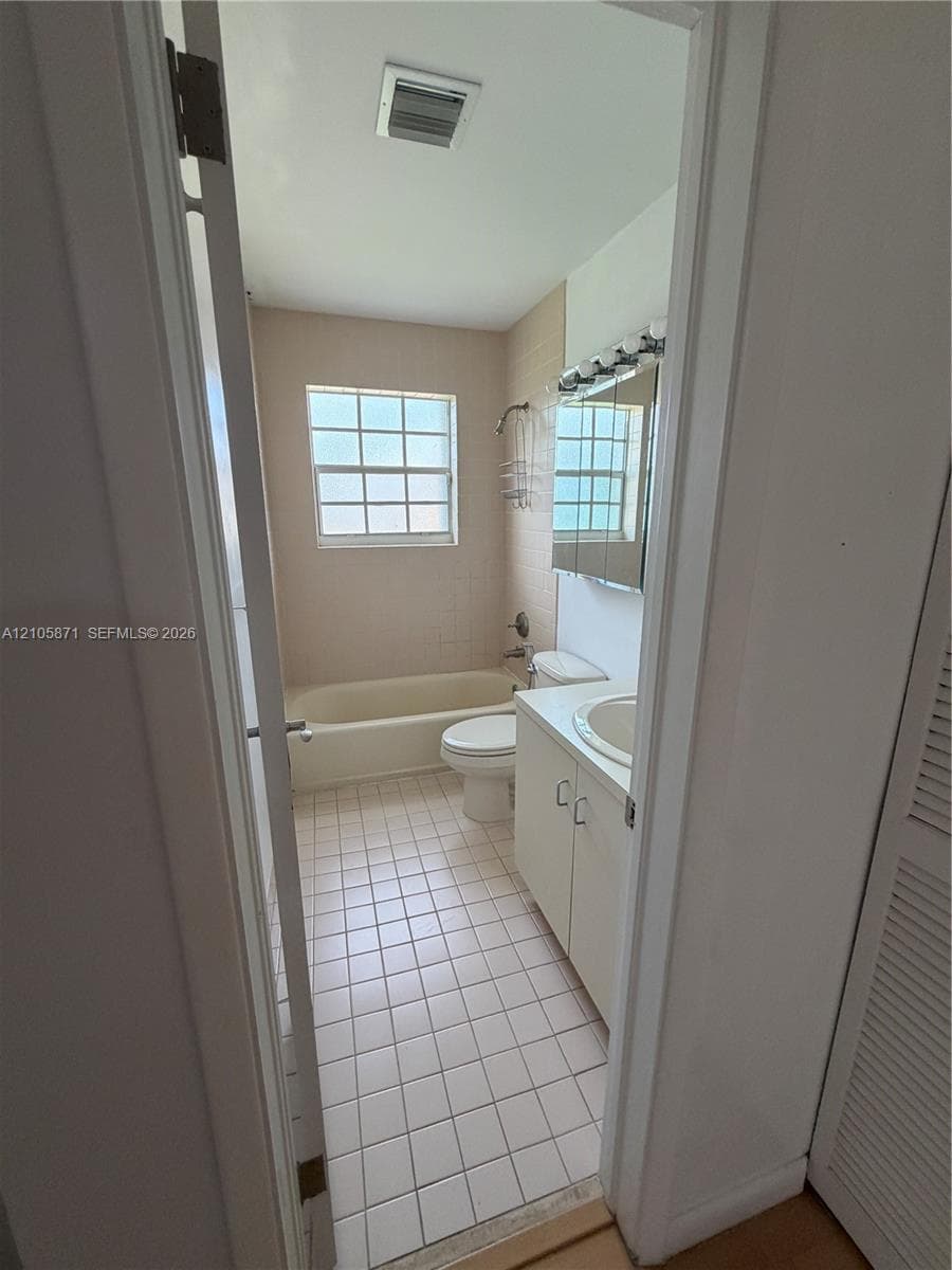 Bathroom featuring ceramic tile flooring, a built-in vanity with a stone countertop and integrated sink, a tiled tub surround, and a multi-light fixture
