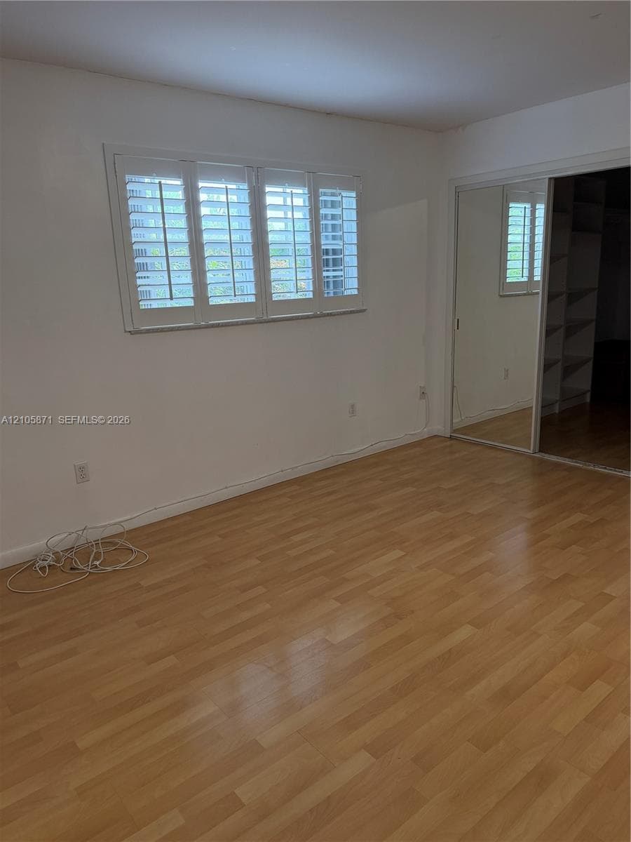 Wood-finish flooring, white plantation shutters, and sliding mirrored closet doors with interior shelving