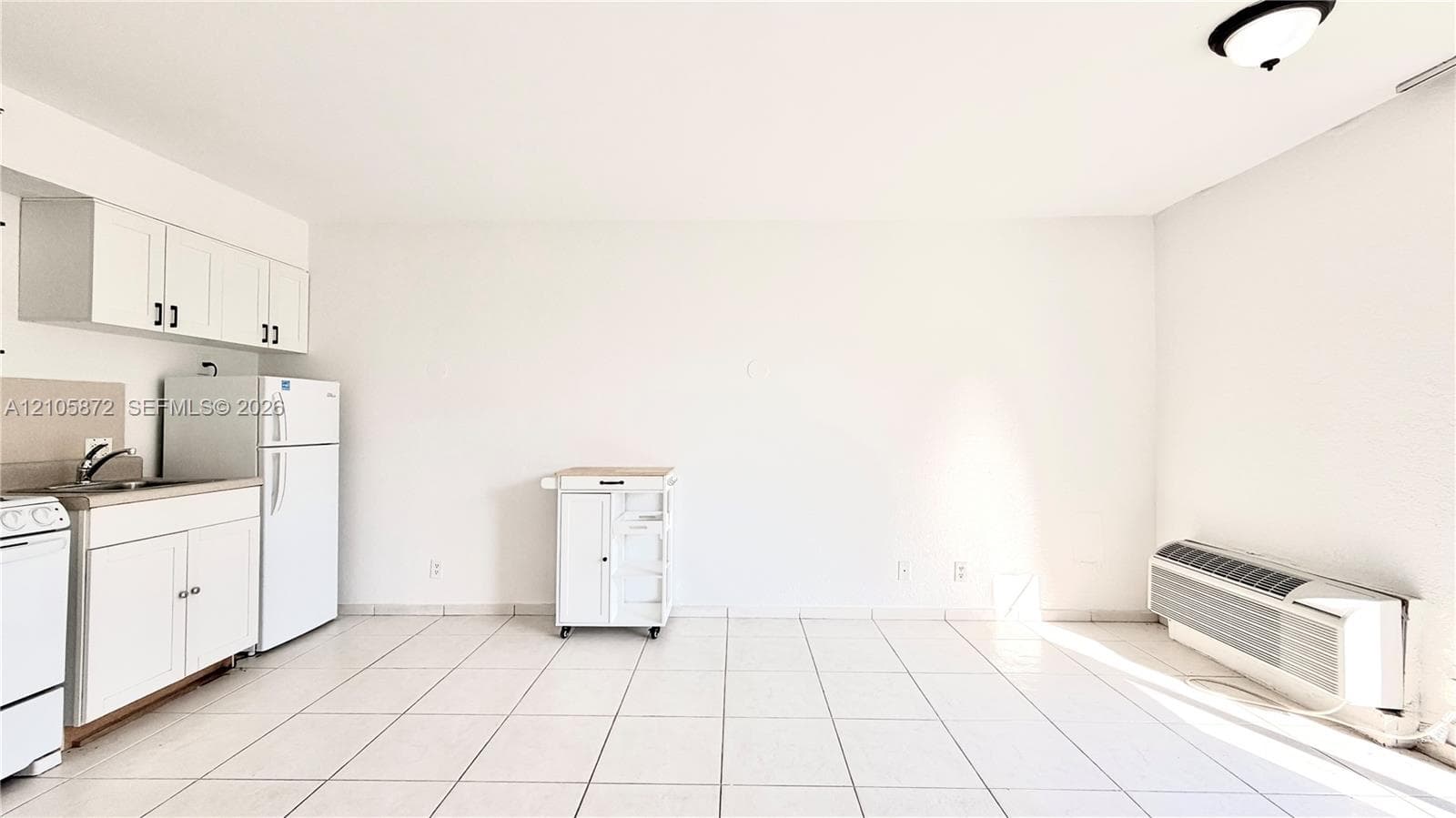 Kitchen area featuring white cabinetry, a neutral-toned backsplash, tile flooring, and a wall-mounted climate control unit