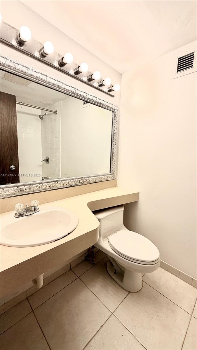 Bathroom featuring a vanity with an integrated basin, large wall-mounted mirror with decorative frame, six-light vanity fixture, and tiled flooring