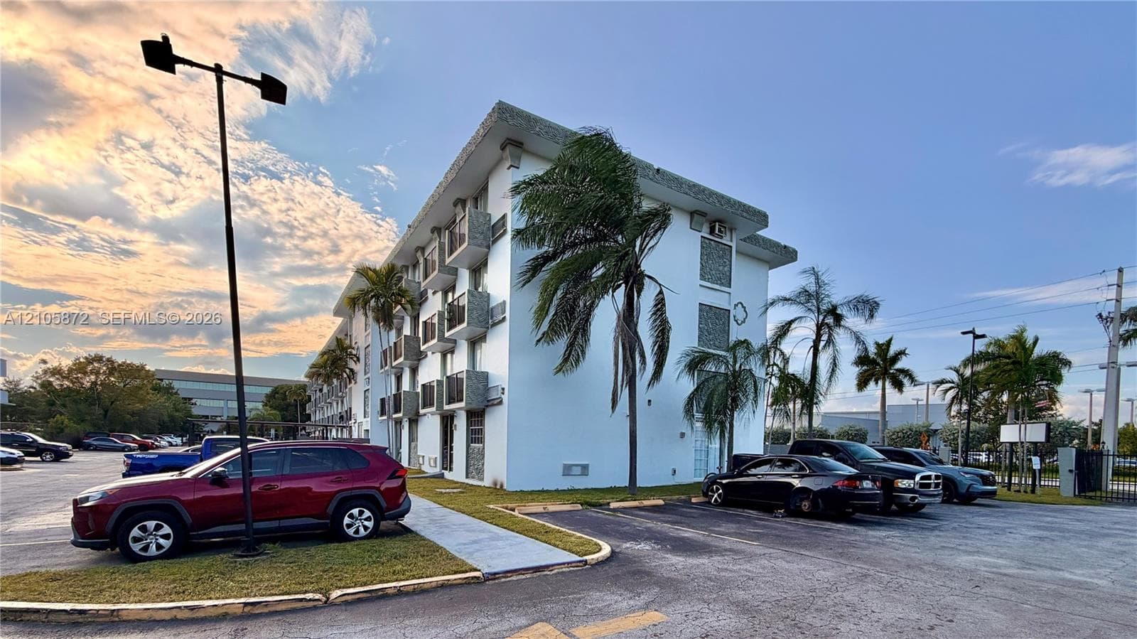 Multi-story building featuring a flat roofline, smooth stucco exterior, individual balconies, and on-site surface parking