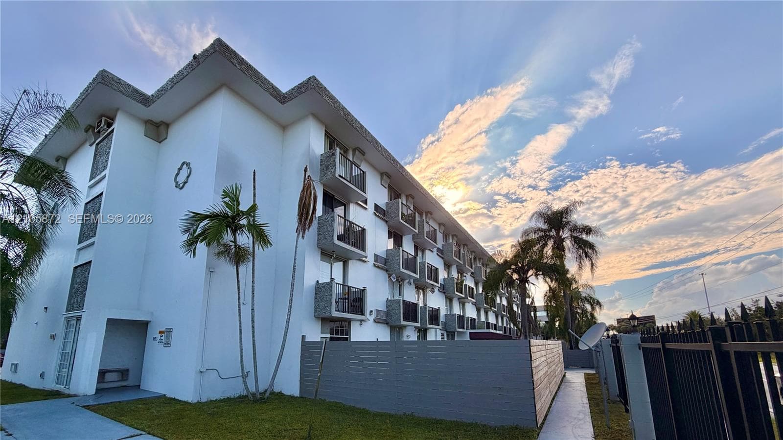 Multi-story exterior featuring white stucco siding, stacked balconies with stone-accented partitions, and integrated perimeter fencing