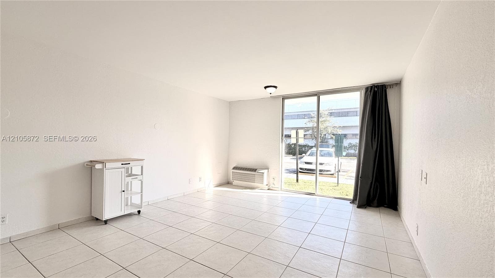 Neutral interior space featuring white tiled flooring, a wall-mounted climate control unit, and a sliding glass door