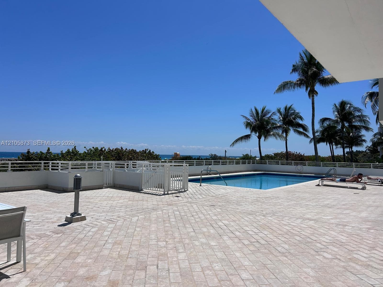 Expansive terrace featuring paved stone flooring, a swimming pool, a perimeter railing, and palm tree scenery