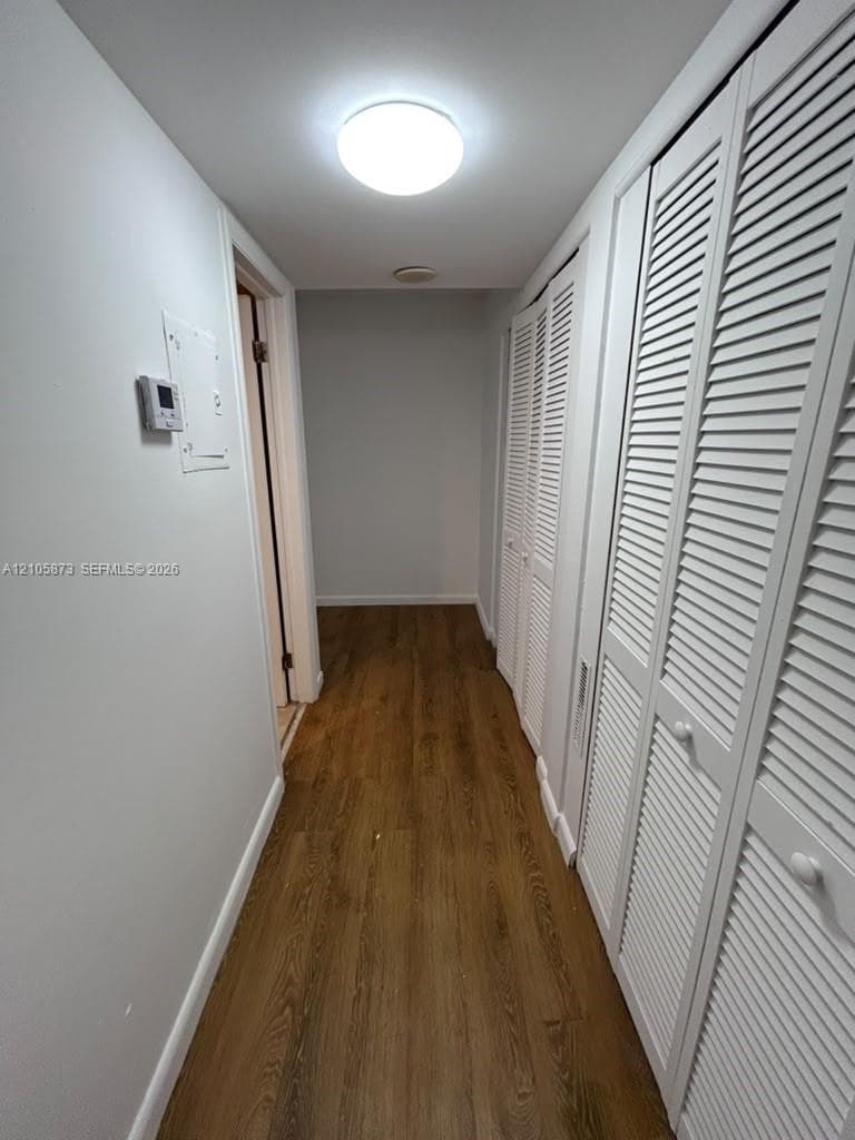 Hallway featuring wood-finish flooring, white louvered closet doors, and a flush-mount ceiling light fixture