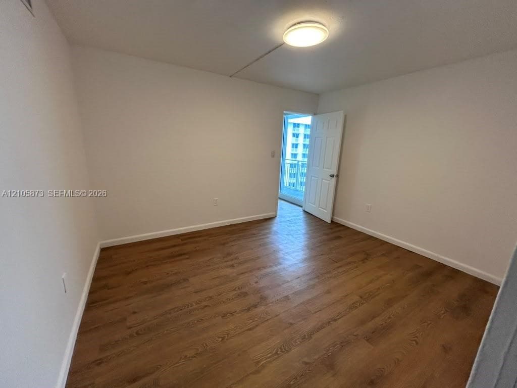 Room featuring wood-finish flooring, a flush-mount ceiling light fixture, a six-panel interior door, and access to an exterior balcony