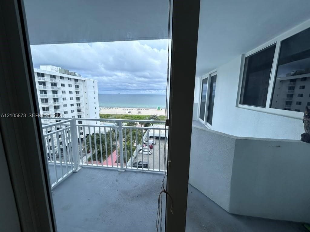Covered balcony featuring white metal railings, concrete flooring, and direct access to the exterior through a glass door