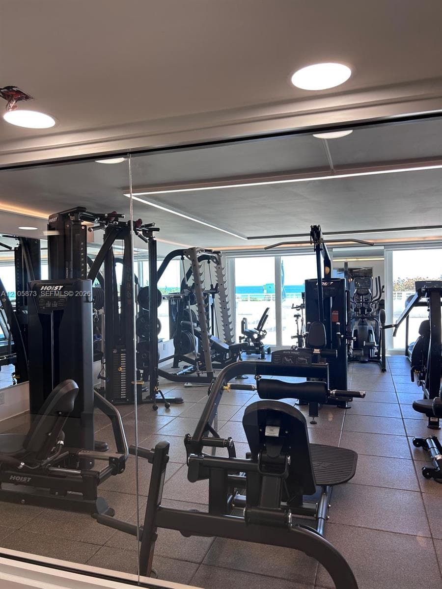 Fitness room featuring expansive wall-to-wall mirrors, recessed ceiling lighting, large-format tile flooring, and floor-to-ceiling glass sliding doors with ocean exposure