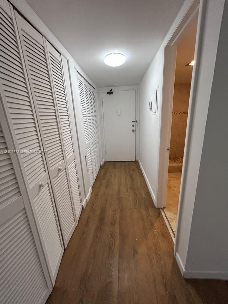Hallway featuring wood-finish flooring, white louvered closet doors, and a flush-mount ceiling light fixture