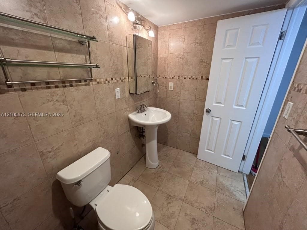 Full-height stone-finish wall tiling with mosaic accent banding, porcelain pedestal sink, mirrored medicine cabinet, and square-format floor tiles
