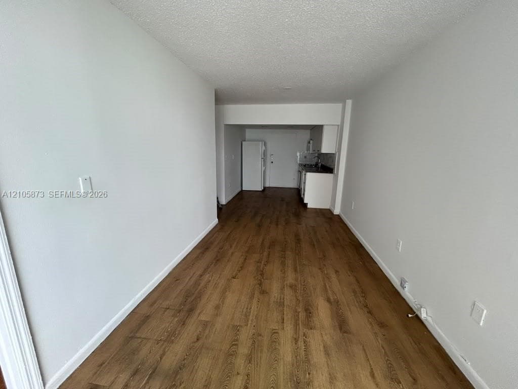 Interior area featuring wood-finish flooring, neutral walls, and a kitchenette equipped with white cabinetry and a built-in refrigerator