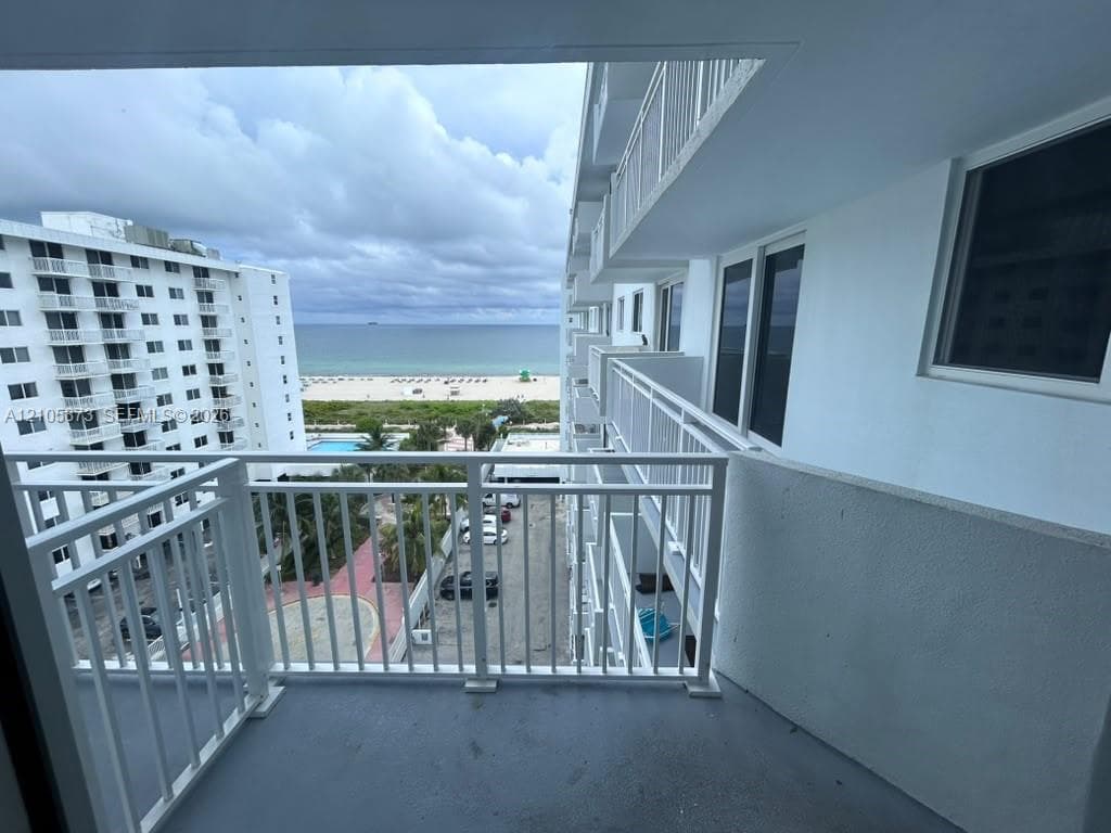 Covered balcony featuring white metal railings, concrete flooring, and direct sightlines to the coastline