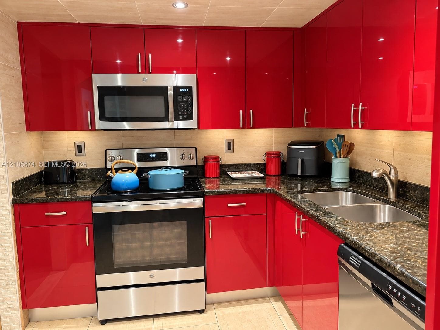 High-gloss red cabinetry, stone countertops, stainless steel appliances, dual-basin sink, and under-cabinet lighting