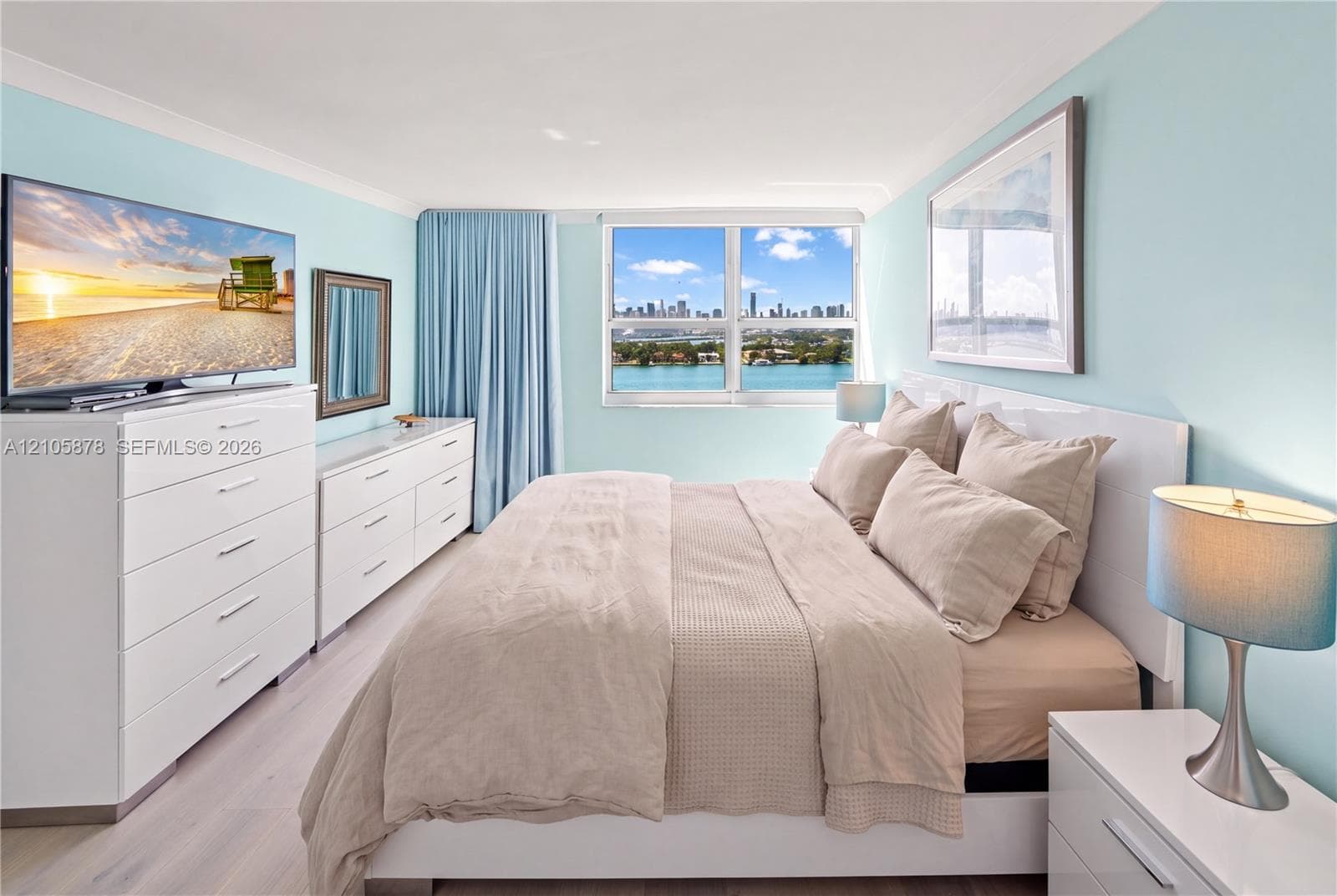 Bedroom featuring light-toned wood-finish flooring, a large window with cityscape and water scenery, and a bright, neutral color palette