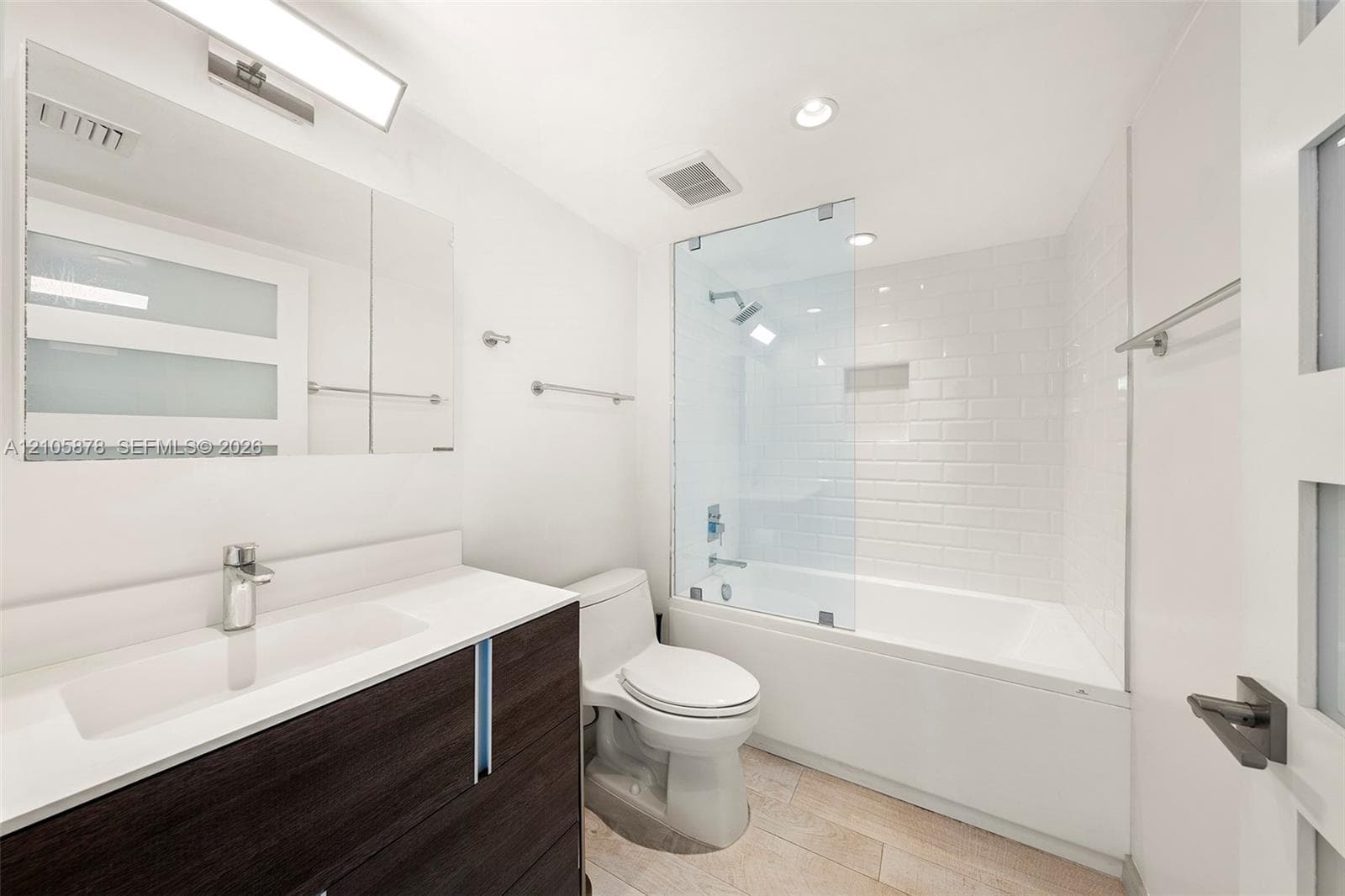 Bathroom featuring a dark-finish wood vanity with a white countertop, subway-tiled shower surround with a glass panel, and light-toned tile flooring