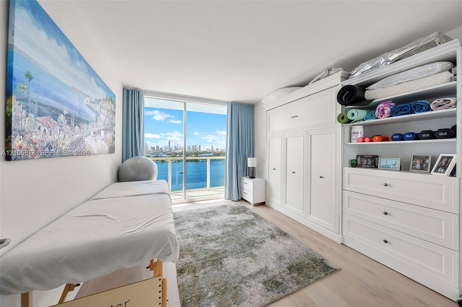 Floor-to-ceiling sliding glass door, custom built-in white cabinetry, wood-finish flooring, and expansive water and skyline backdrop
