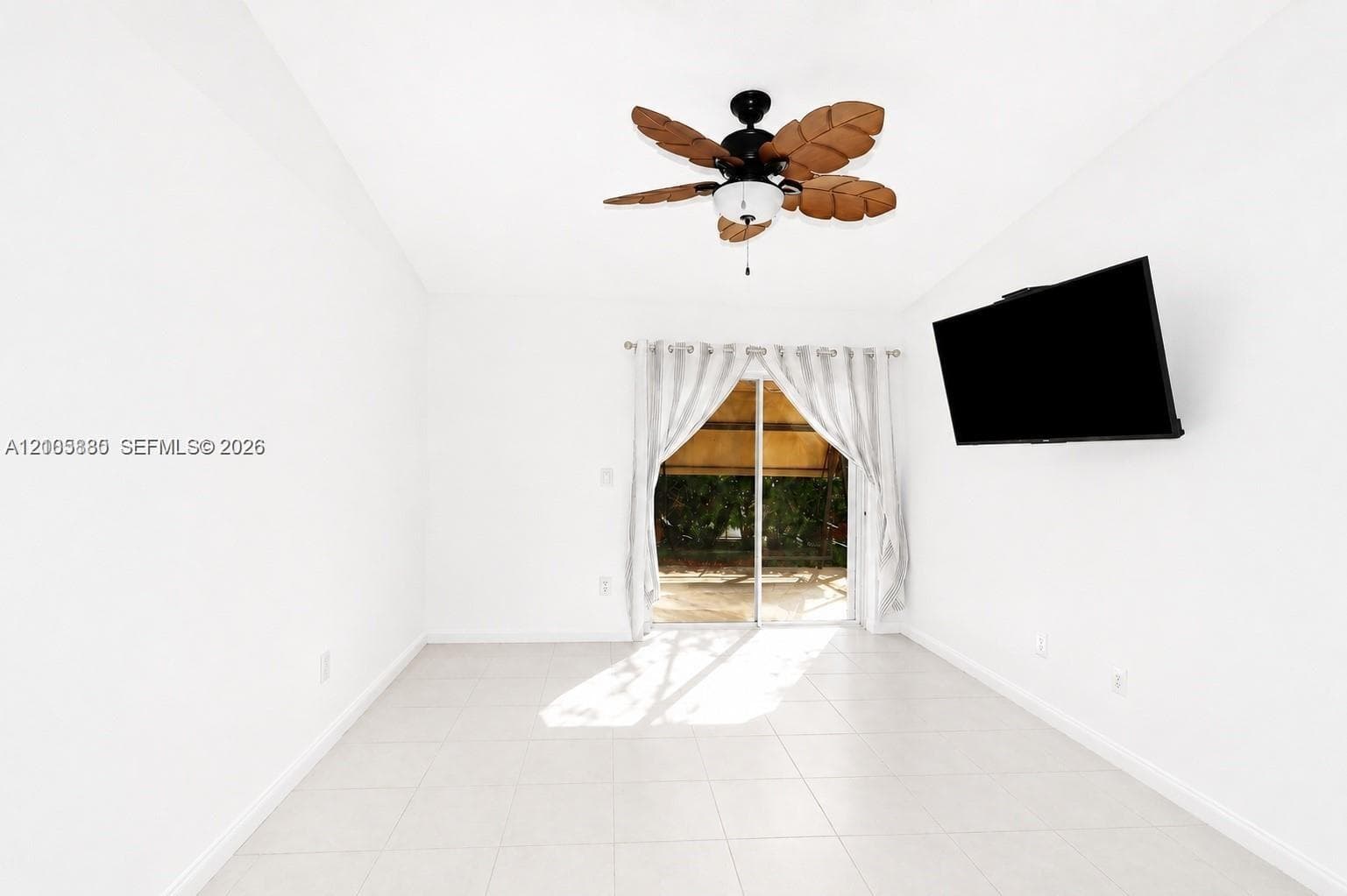 Light-filled room featuring large-format tile flooring, a palm-leaf style ceiling fan, and sliding glass doors