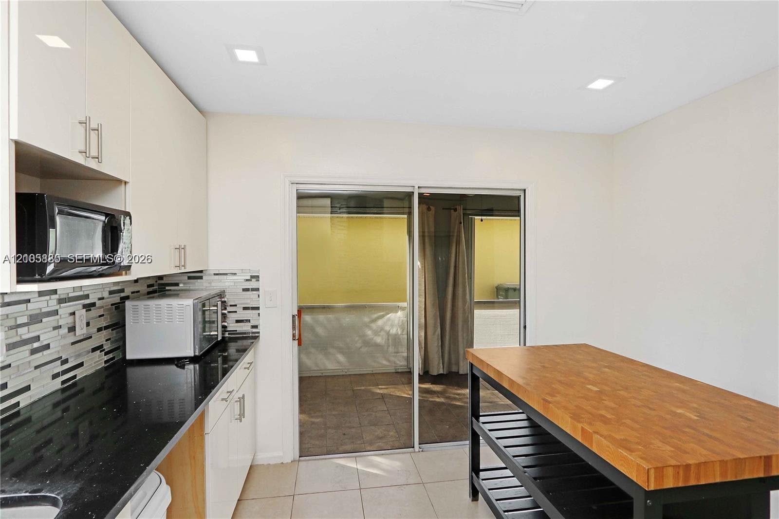 Kitchen featuring flat-panel cabinetry, black countertops, multi-toned mosaic tile backsplash, recessed lighting, and sliding glass doors