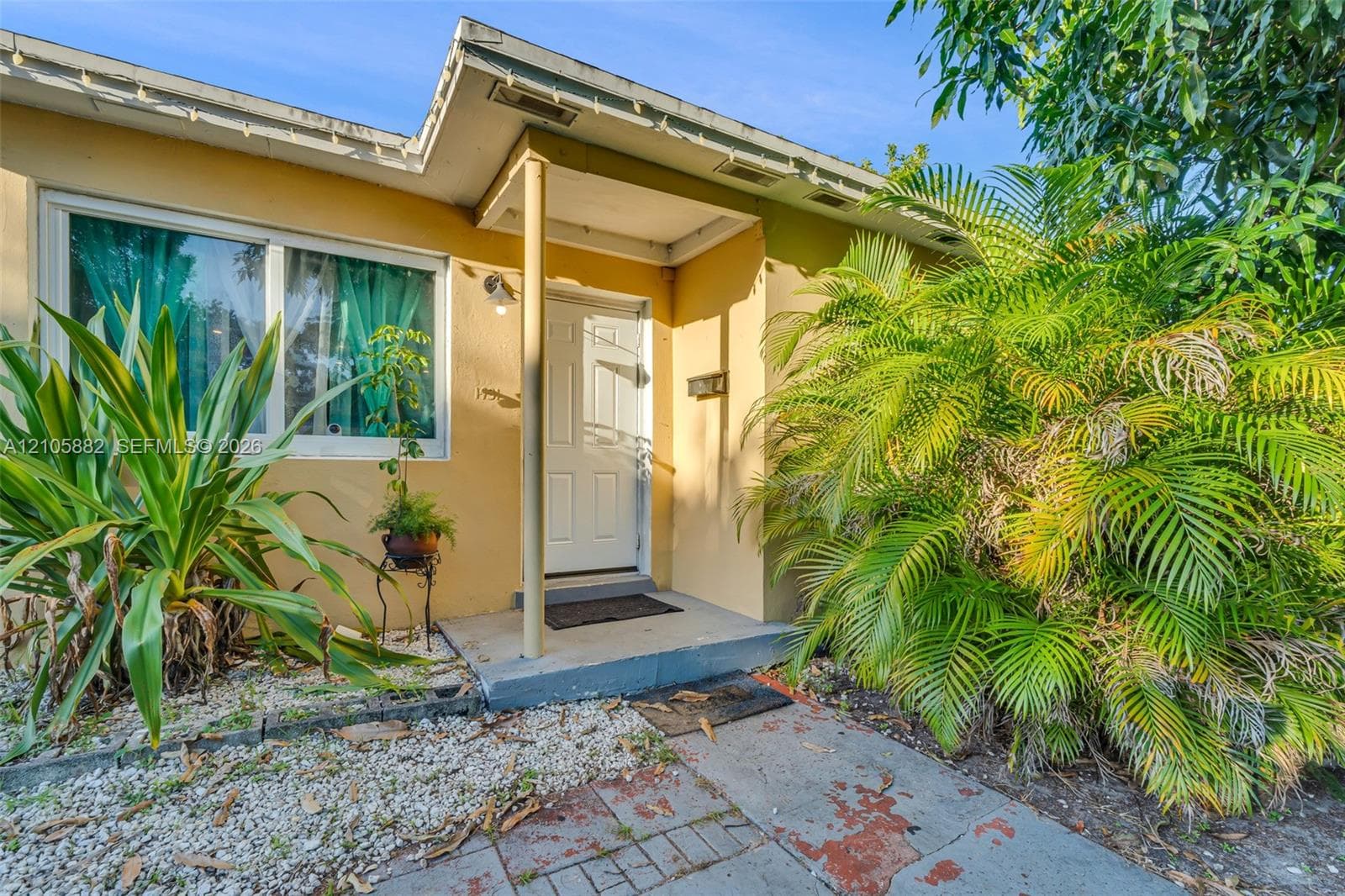 Exterior entryway featuring a white paneled door, covered porch, large single-hung window, and stone-accented landscaping
