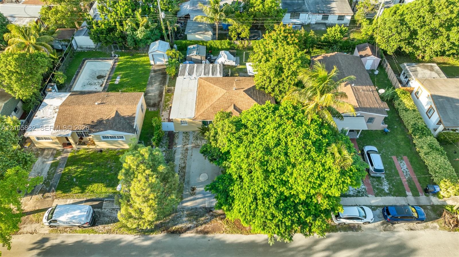 Aerial view featuring a residential property with a detached storage structure, concrete driveway, and a backyard pool