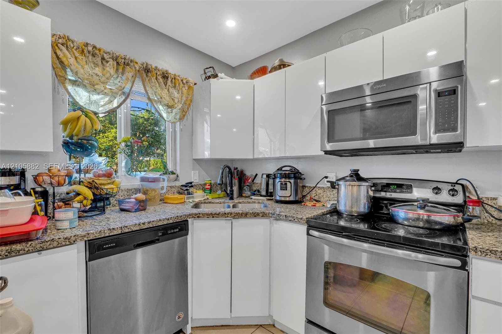 Kitchen featuring white high-gloss cabinetry, stone-finish countertops, stainless steel appliances, a dual-basin sink, and recessed lighting