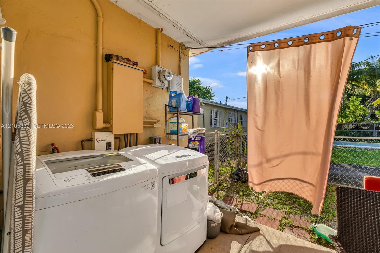 Covered outdoor laundry area with concrete flooring, chain-link perimeter fencing, and exterior electrical service components