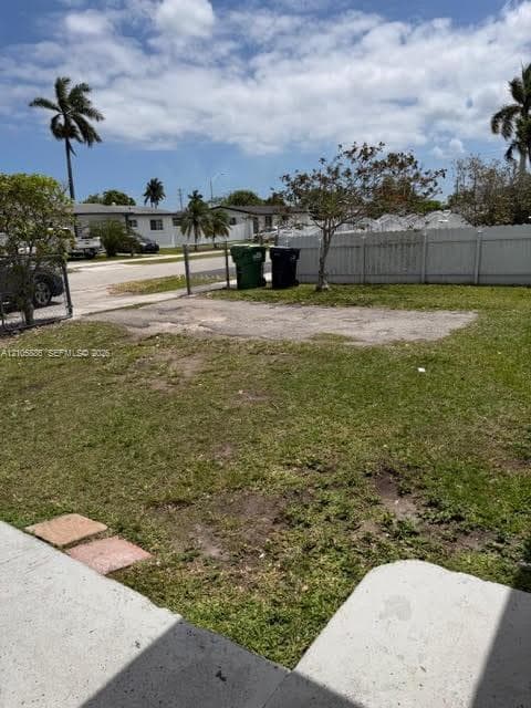 Outdoor space featuring a fenced perimeter, concrete paved area, and mature palm trees