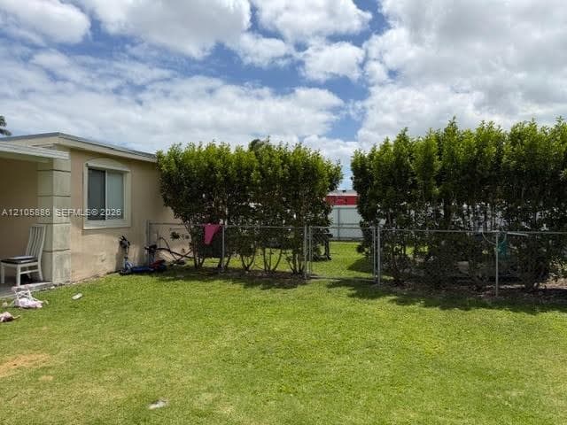Rear yard featuring a manicured lawn, chain-link fencing, and mature perimeter hedges